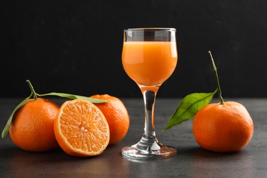 Photo of Delicious tangerine liqueur in glass and fresh fruits on grey table