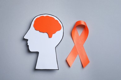 Photo of Human head cutout, brain and orange ribbon on grey background, flat lay. Multiple sclerosis concept