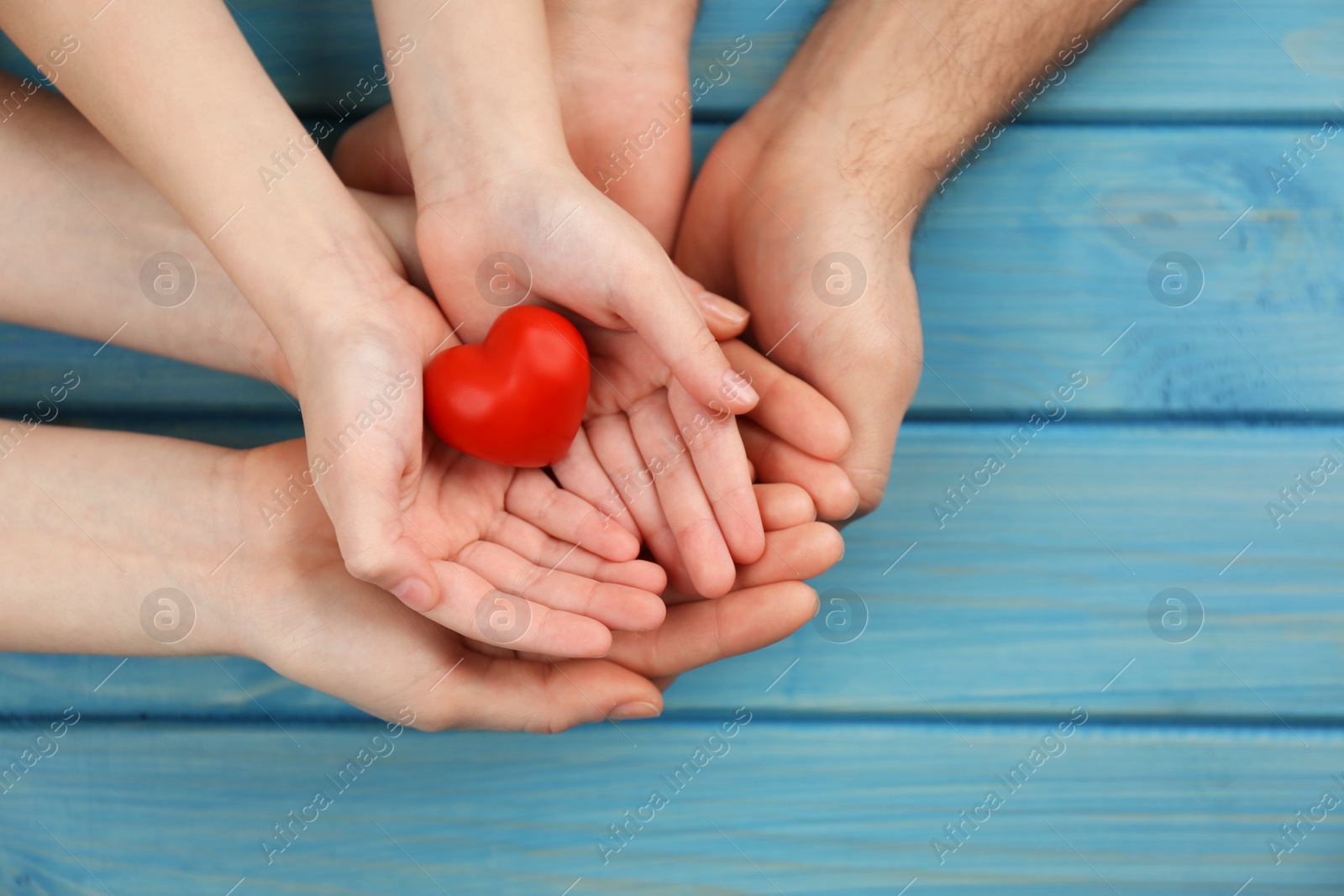 Photo of Parents and kid holding red heart in hands at turquoise wooden table, top view. Family day