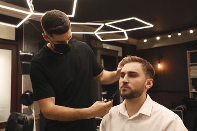 Professional hairdresser working with client in barbershop