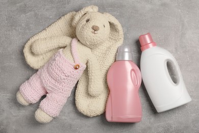 Bottles of laundry detergents and rabbit toy on light grey table, flat lay