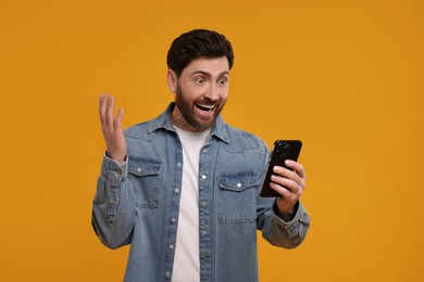 Photo of Emotional man with smartphone on orange background