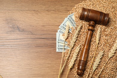 Photo of Agricultural business. Dollar banknotes, judge's gavel, wheat ears and grains on wooden table, flat lay. Space for text