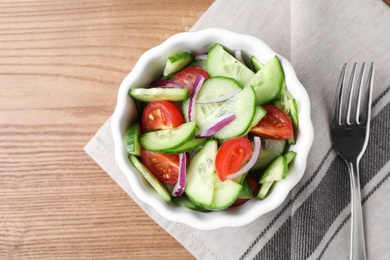 Photo of Bowl of tasty cucumber tomato salad served on wooden table, flat lay