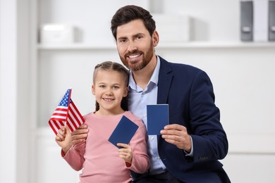 Photo of Immigration. Happy man with his daughter holding passports and American flag indoors