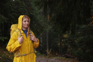 Photo of Young woman with raincoat and backpack in forest under rain