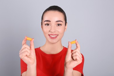 Young woman with foam ear plugs on grey background