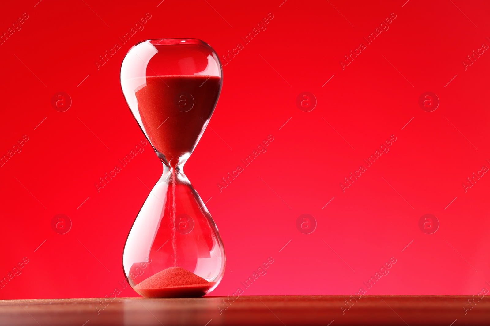 Photo of Hourglass with flowing sand against red background. Space for text