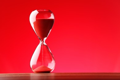 Hourglass with flowing sand against red background. Space for text