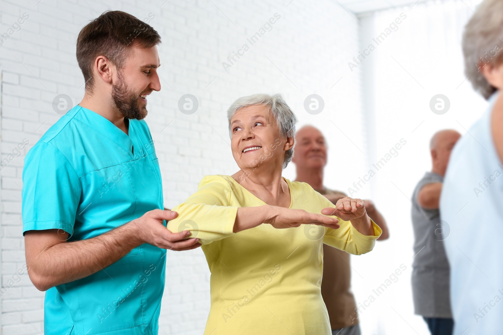 Photo of Care worker helping elderly woman to do sports exercise in hospital gym.
