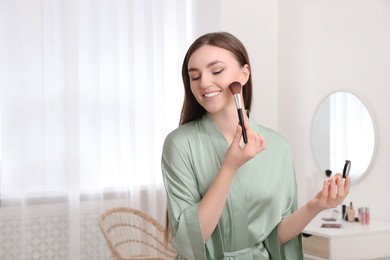 Photo of Beautiful young woman applying makeup with brush at home. Space for text