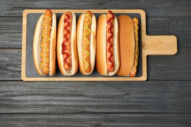 Photo of Board with hot dogs on wooden table, top view. Space for text