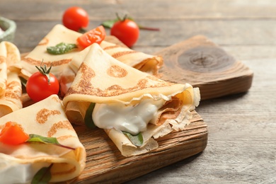 Photo of Thin pancakes with sour cream and cherry tomatoes on wooden board