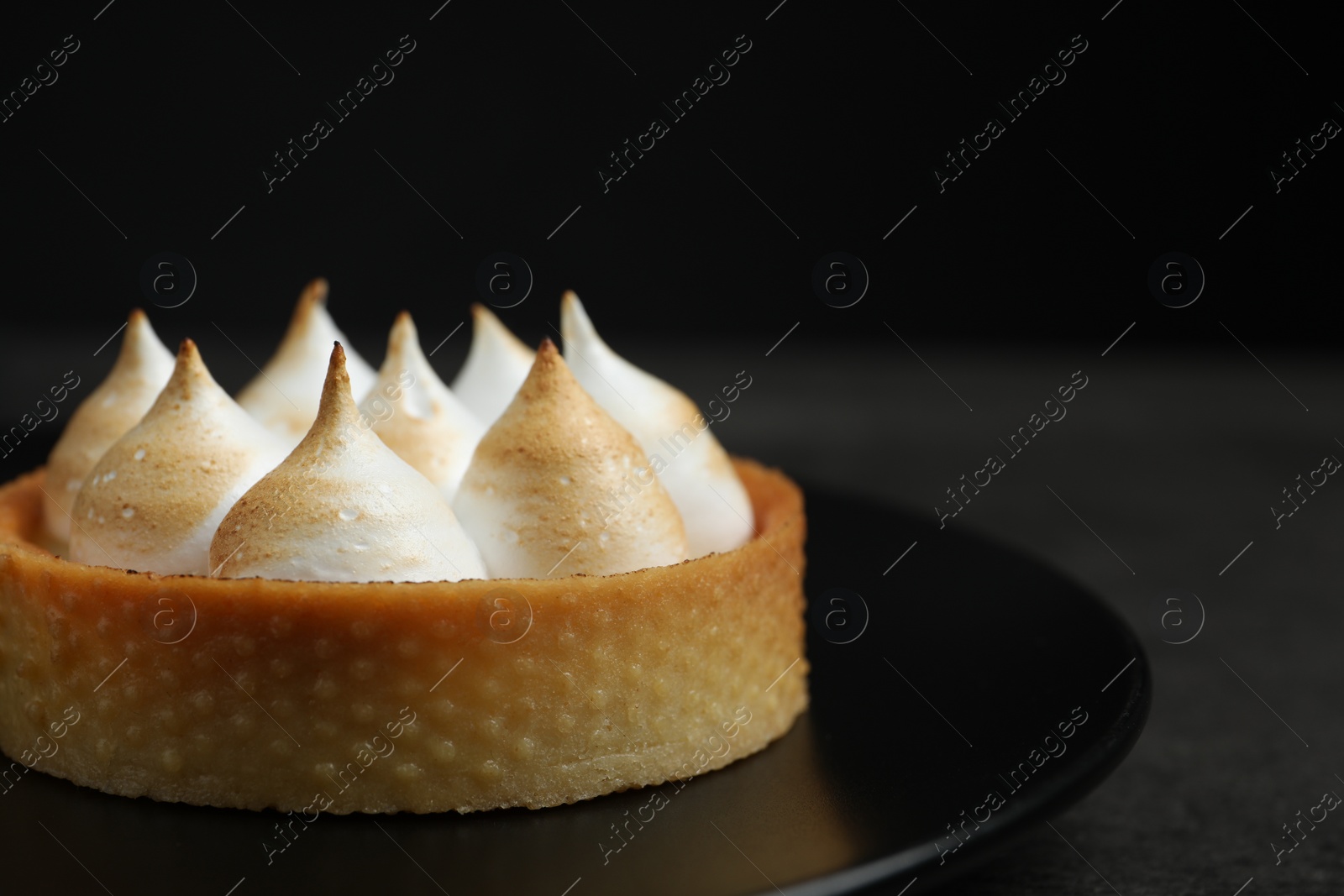 Photo of Tartlet with meringue on black table, closeup and space for text. Delicious dessert