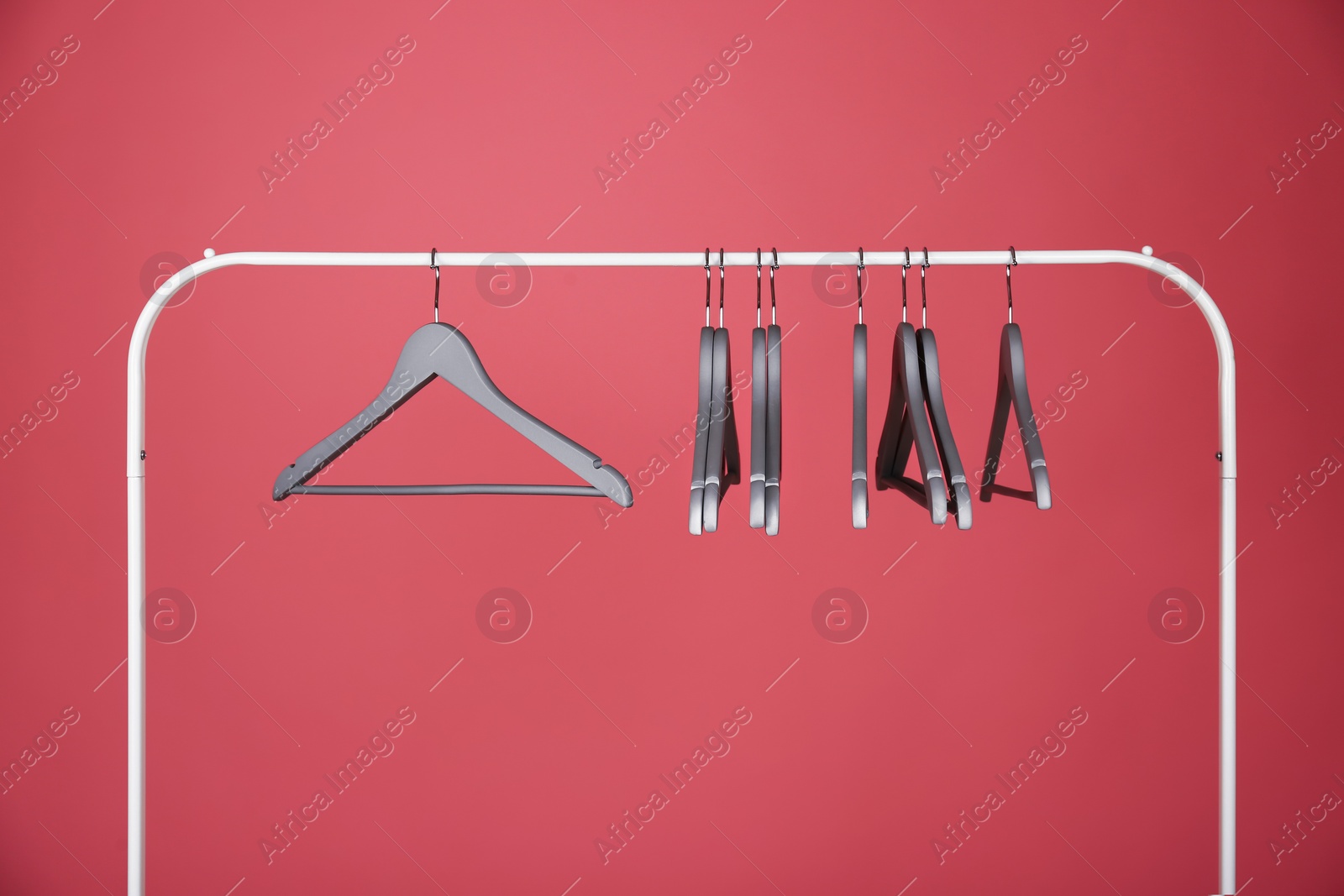 Photo of Empty clothes hangers on metal rack against color background