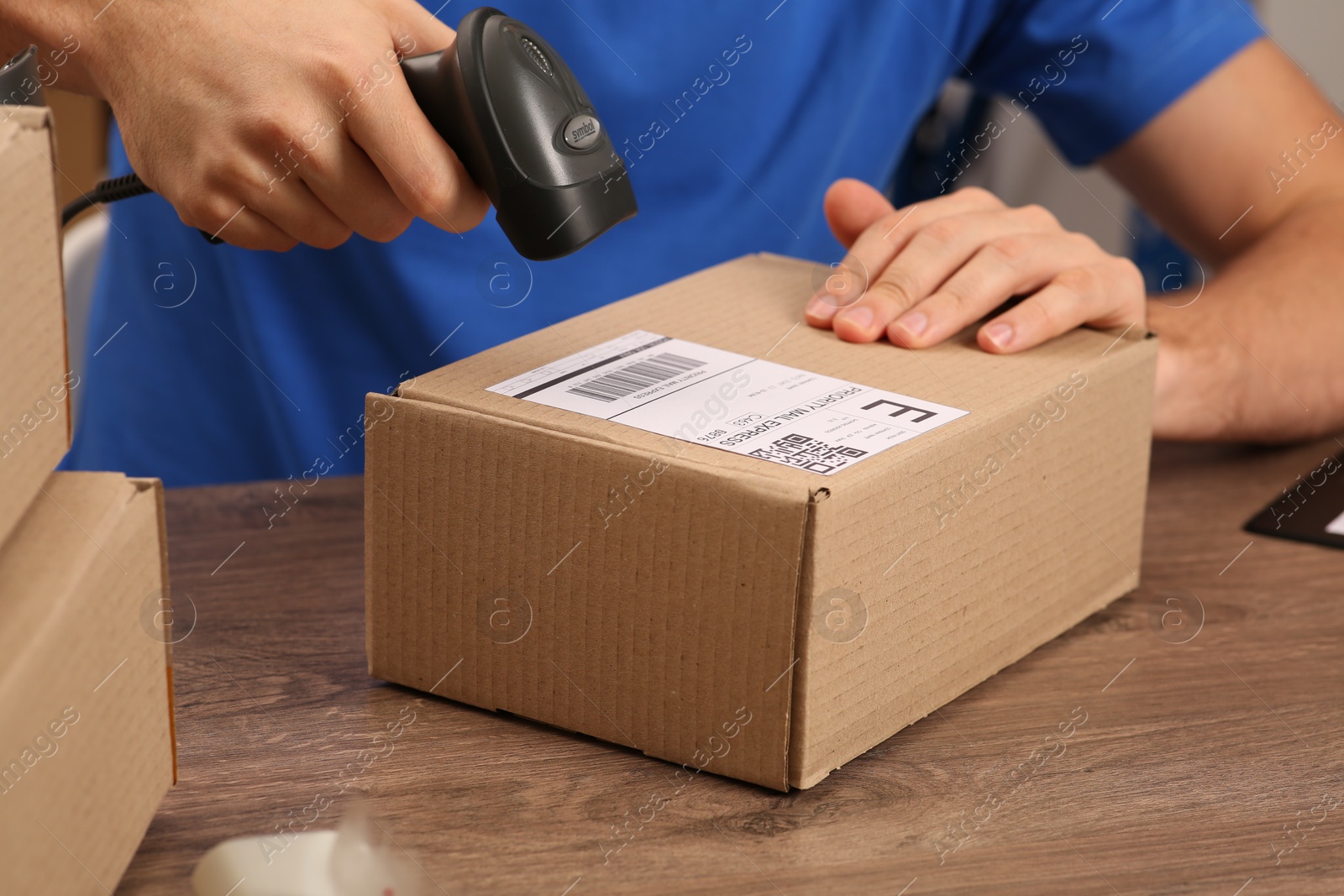 Photo of Post office worker with scanner reading parcel barcode at counter, closeup