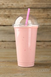 Photo of Plastic cup of tasty smoothie on wooden table