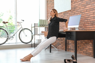 Photo of Young businesswoman stretching at workplace. Productivity boost