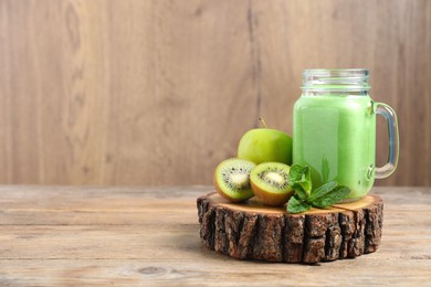 Tasty fresh green smoothie in mason jar near ingredients on wooden table, space for text