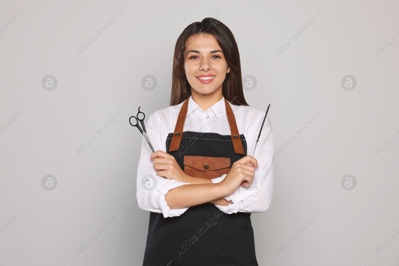 Photo of Portrait of happy hairdresser with professional scissors and comb against light grey background
