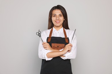 Photo of Portrait of happy hairdresser with professional scissors and comb against light grey background