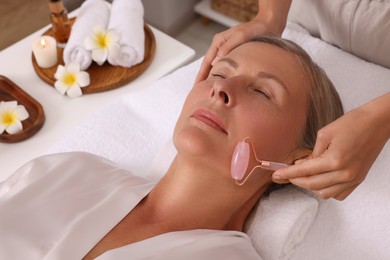 Photo of Woman receiving facial massage with rose quartz roller in beauty salon, closeup