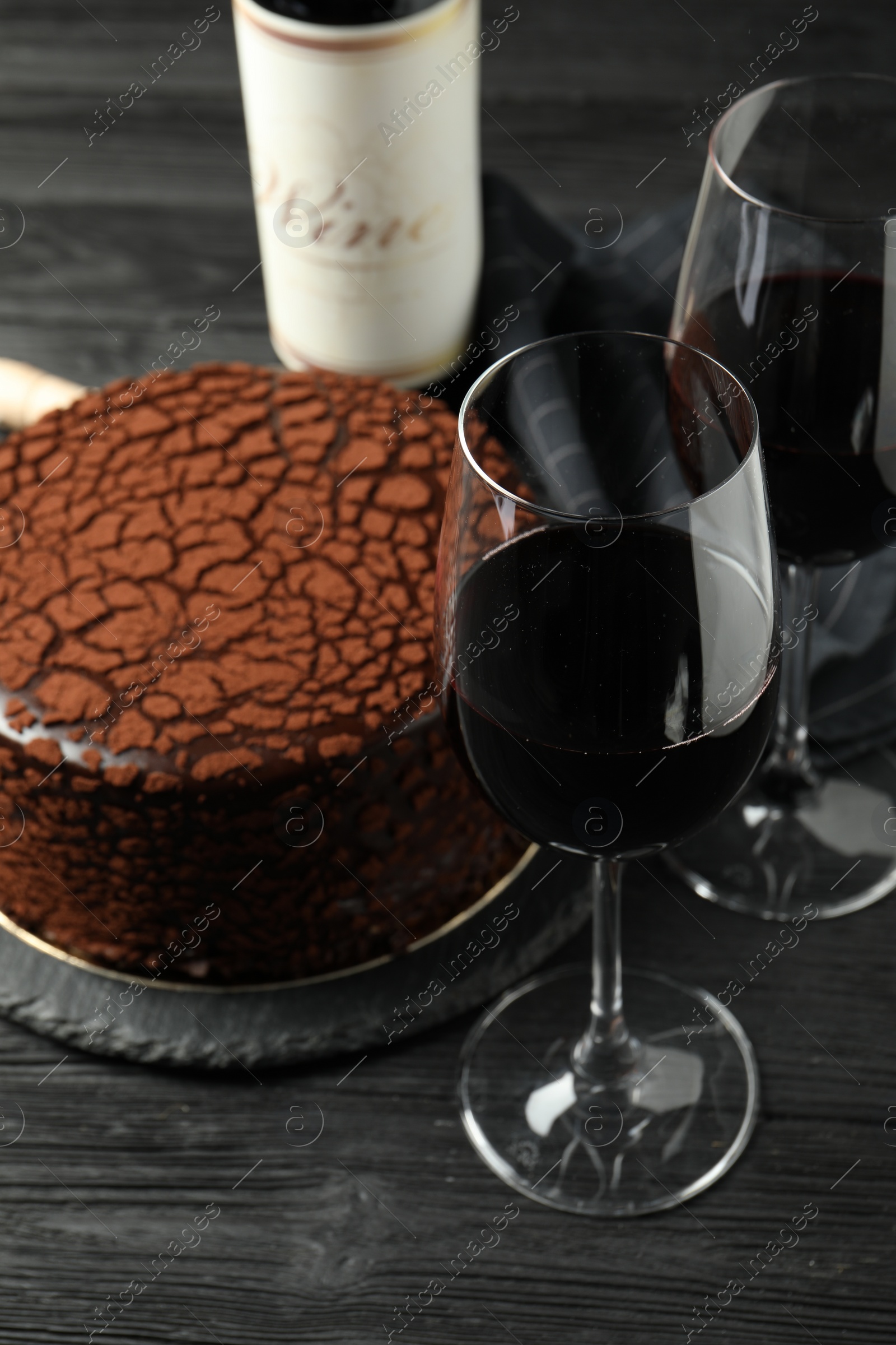 Photo of Delicious chocolate truffle cake and red wine on black wooden table