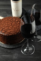 Photo of Delicious chocolate truffle cake and red wine on black wooden table