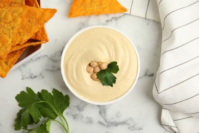 Photo of Delicious hummus with nachos on white marble table, flat lay