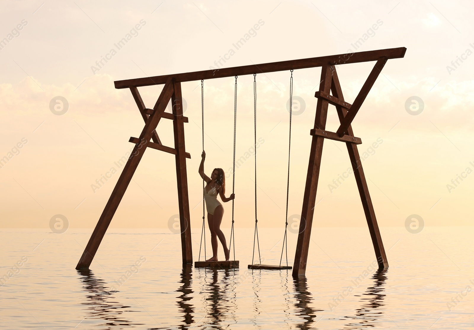 Photo of Young woman enjoying sunrise on swing over water