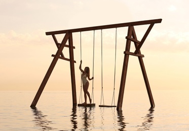 Photo of Young woman enjoying sunrise on swing over water