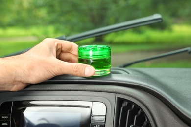 Photo of Man putting air freshener on dashboard in car, closeup