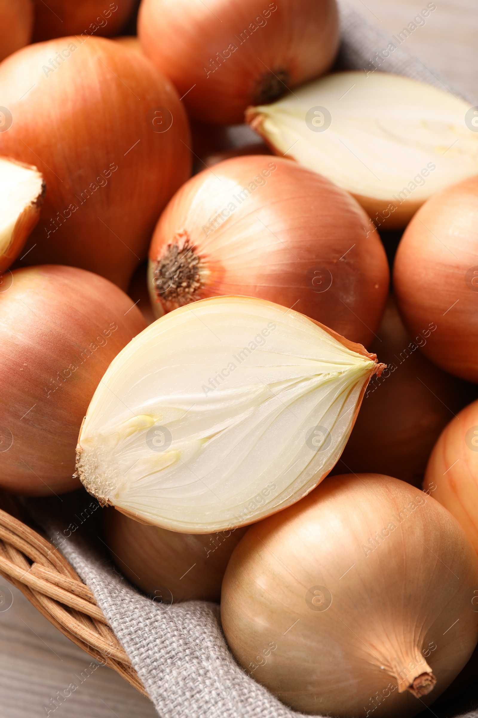 Photo of Wicker basket with whole and cut onions on wooden table, closeup