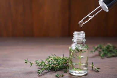 Photo of Dripping thyme essential oil into bottle on wooden table, space for text