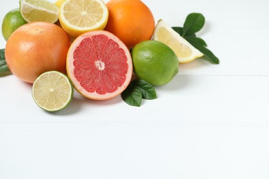 Photo of Different fresh citrus fruits and leaves on white wooden table. Space for text