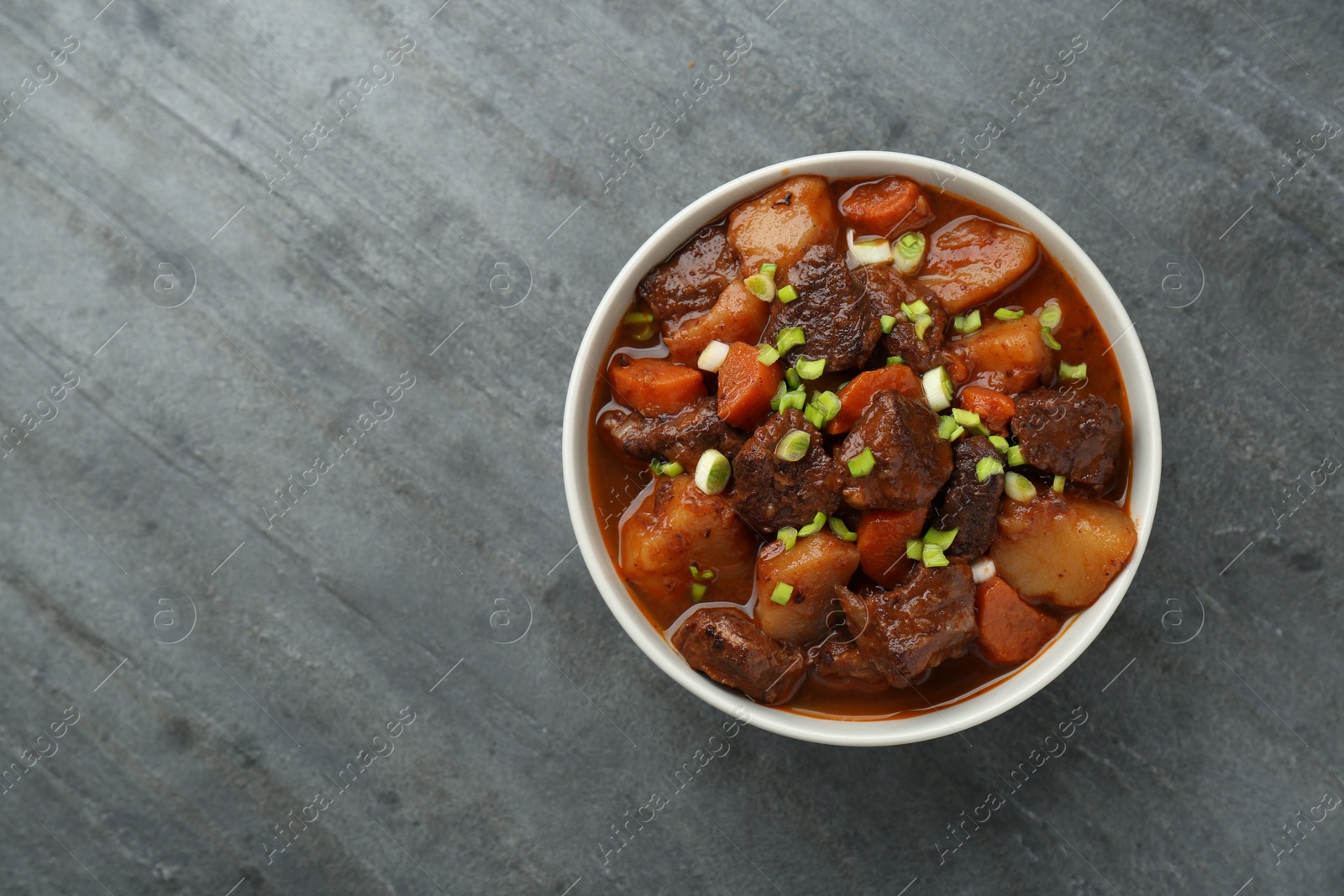 Photo of Delicious beef stew with carrots, green onions and potatoes on grey table, top view. Space for text