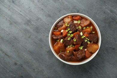 Delicious beef stew with carrots, green onions and potatoes on grey table, top view. Space for text