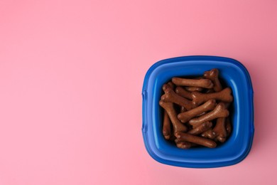 Photo of Blue bowl with bone shaped dog cookies on pink background, top view. Space for text