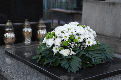 Photo of Funeral wreath of flowers and grave lanterns on granite tombstone in cemetery