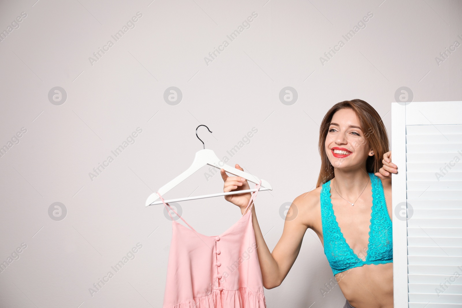 Photo of Young woman with clothes on hanger behind folding screen against light background, space for text. Dressing room