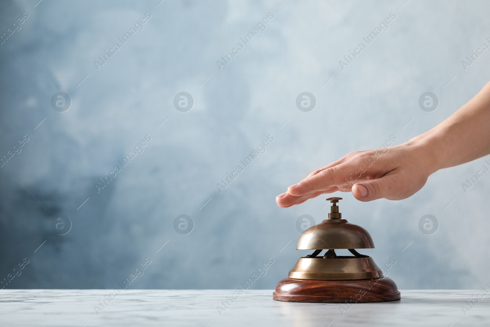 Photo of Man ringing hotel service bell at table on blue background, closeup. Space for text