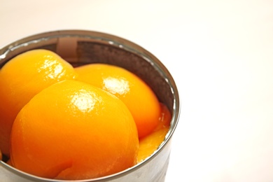 Open tin can of peaches on beige background, closeup. Space for text