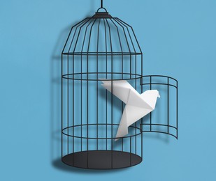 Image of Freedom. Paper bird flying out of broken cage on light blue background