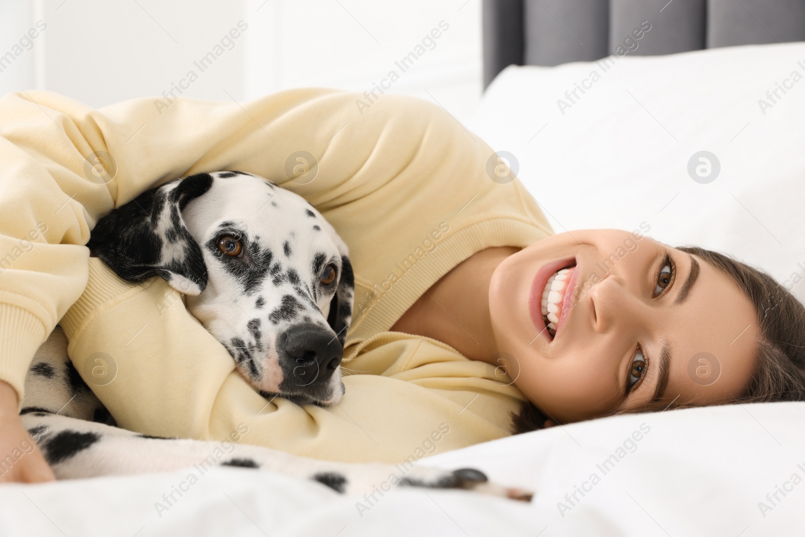 Photo of Beautiful woman with her adorable Dalmatian dog on bed at home. Lovely pet