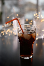 Photo of Glass of cold cola and fairy lights on table