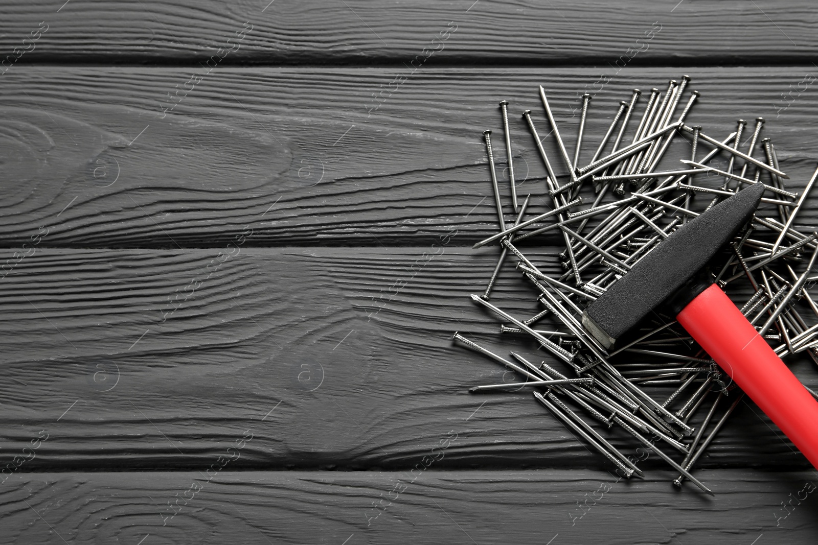 Photo of Hammer and metal nails on black wooden table, flat lay. Space for text