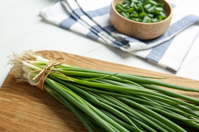 Photo of Fresh green spring onions on wooden board, closeup