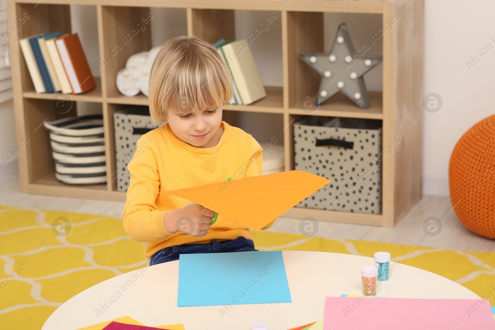 Photo of Cute little boy cutting orange paper at desk in room. Home workplace