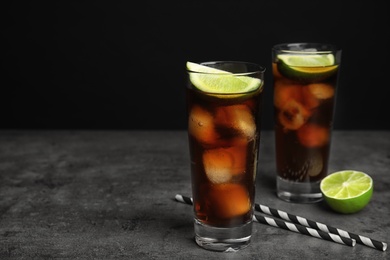 Photo of Refreshing soda drinks with straws on grey table against black background, space for text