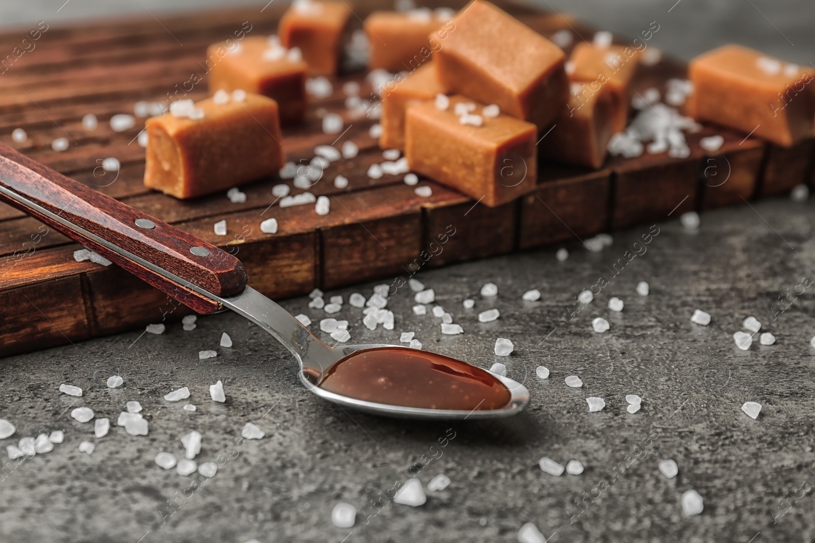 Photo of Spoon with delicious caramel sauce, salt and candies on table